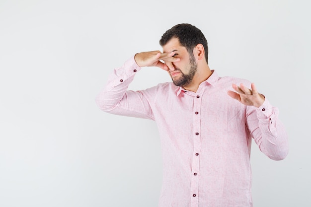 Jeune homme se pinçant le nez en raison d'une mauvaise odeur en chemise rose et à la dégoûté