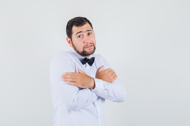 Jeune homme se serrant dans ses bras ou se sentir froid en chemise blanche et à la vue de face impuissante.