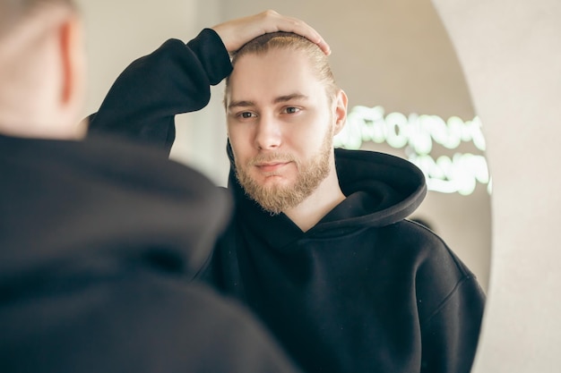 Photo gratuite un jeune homme séduisant avec une barbe se regarde dans le miroir