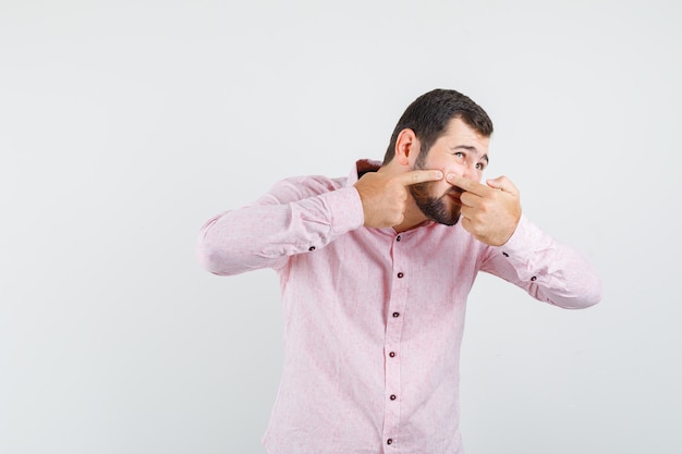 Photo gratuite jeune homme serrant le bouton sur la joue en chemise rose et à l'irritation