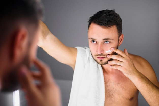 Jeune homme avec une serviette sur son épaule en regardant dans le miroir