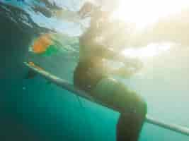 Photo gratuite jeune homme en short assis sur une planche de surf dans l'océan