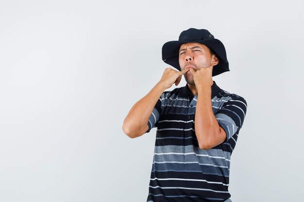 Jeune homme sifflant avec les doigts en t-shirt, vue de face de chapeau.