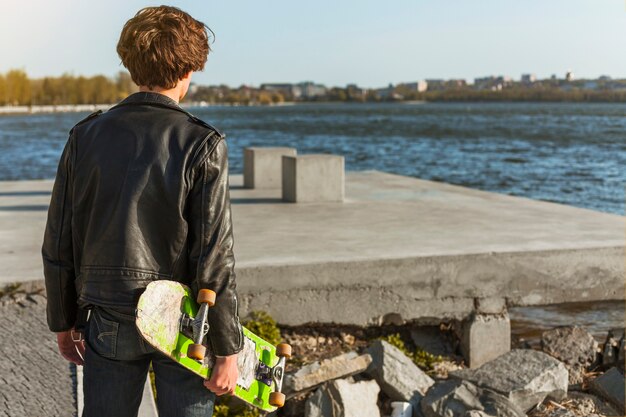 Photo gratuite jeune homme avec un skateboard près de la mer