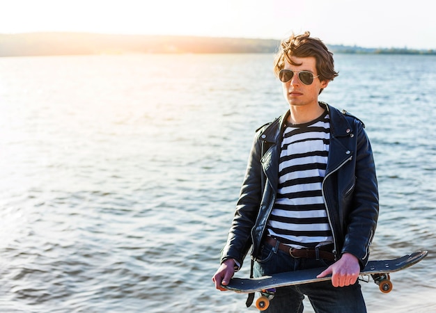 Photo gratuite jeune homme avec un skateboard près de la mer