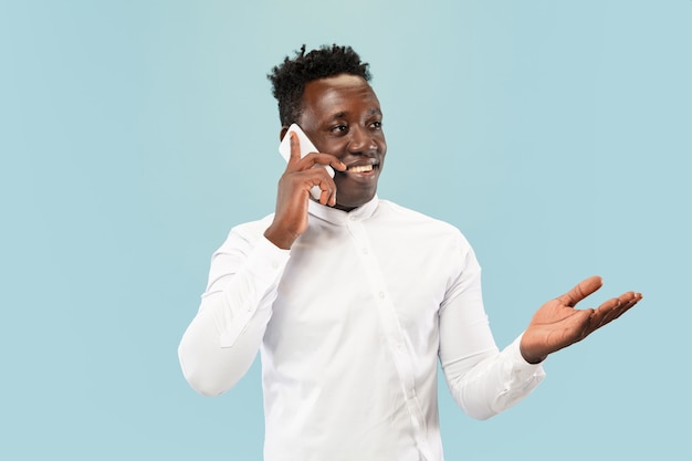 Jeune homme avec smartphone isolé sur mur bleu studio