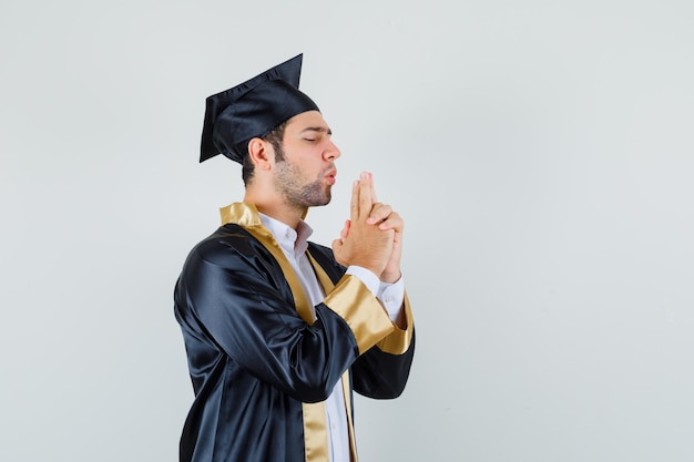 Jeune homme soufflant sur le pistolet à doigt en uniforme diplômé et à la confiance. vue de face.