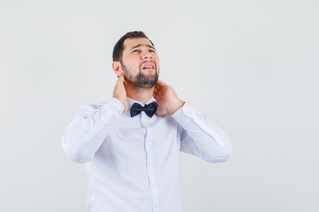 Jeune homme souffrant de douleurs au cou en chemise blanche et à la fatigue. vue de face.