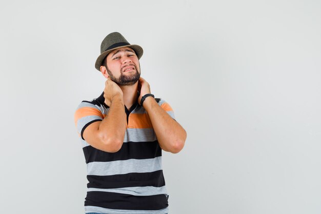 Jeune homme souffrant de douleurs au cou en t-shirt, chapeau et à l'ennui.