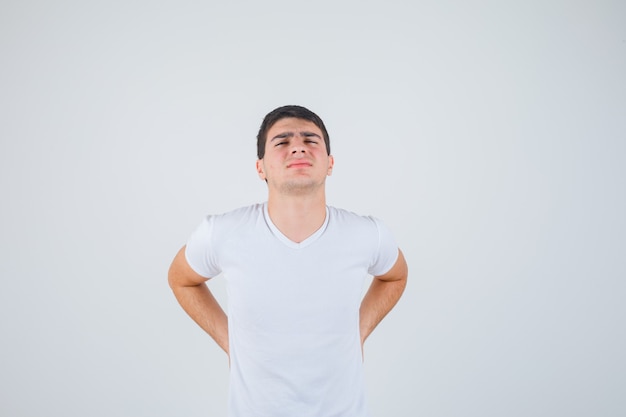 Photo gratuite jeune homme souffrant de douleurs lombaires en t-shirt et à la recherche de mal, vue de face.