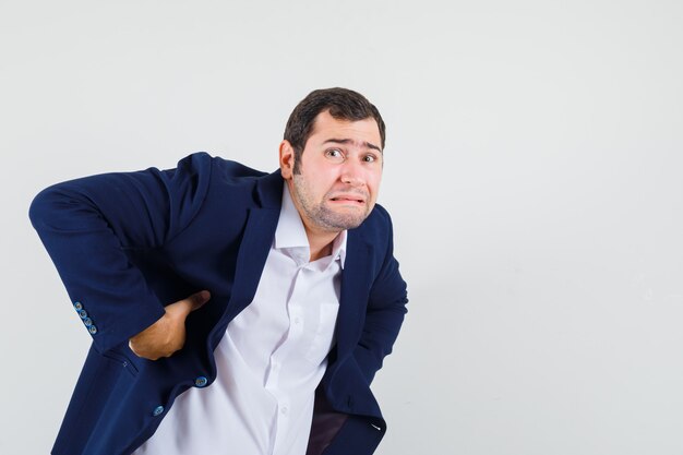 Jeune homme souffrant de maux de dos en chemise, veste et à la fatigue