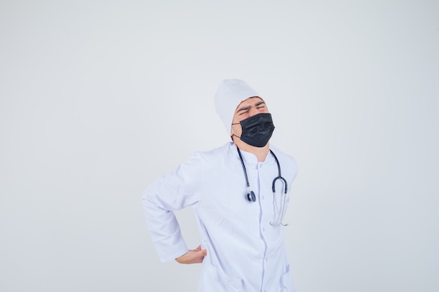 Jeune homme souffrant de maux de dos en uniforme blanc, masque et à la douleur. vue de face.