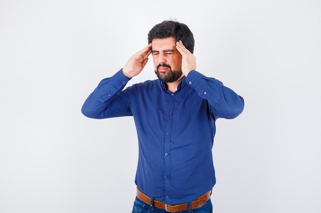 Jeune homme souffrant de maux de tête en chemise bleue et ayant l'air fatigué, vue de face.