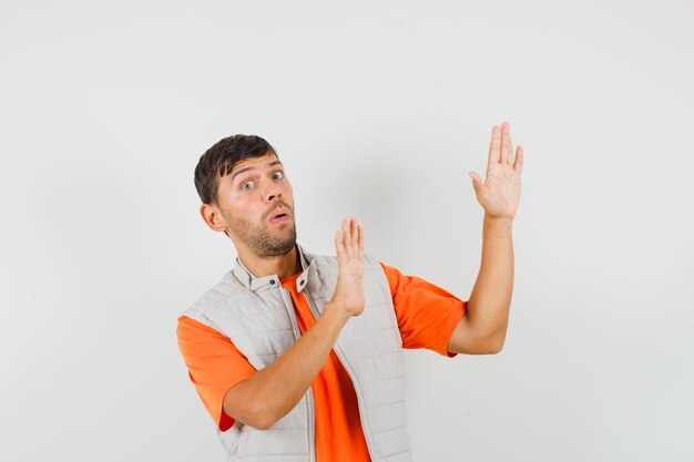 Jeune homme soulevant des paumes de manière protectrice en t-shirt, veste et à la peur