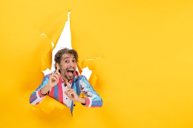 Un jeune homme souriant et émotif, satisfait, pose sur fond de trou de papier jaune déchiré