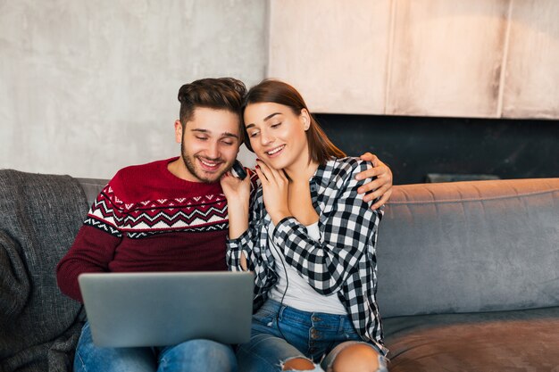 Jeune homme souriant et femme assise à la maison en hiver, tenant un ordinateur portable, écoutant des écouteurs, étudiants qui étudient en ligne, couple sur le temps libre ensemble, heureux, émotion positive, rencontres