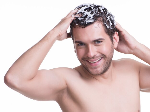 Jeune homme souriant heureux, laver les cheveux avec du shampoing - isolé sur blanc.