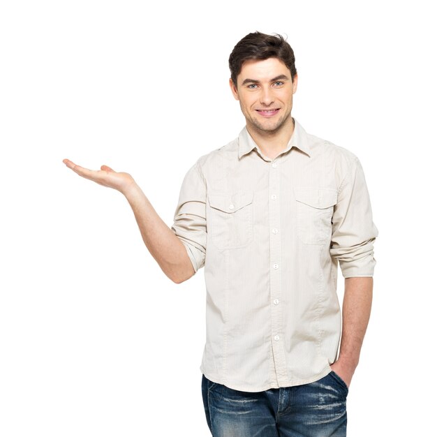 Jeune homme souriant montre quelque chose sur la paume isolée sur le mur blanc.