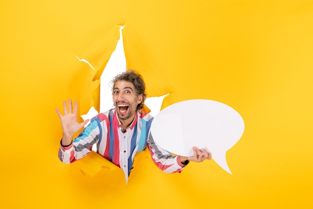 Photo gratuite jeune homme souriant pointant une page blanche avec un espace libre et montrant cinq dans un trou déchiré dans du papier jaune