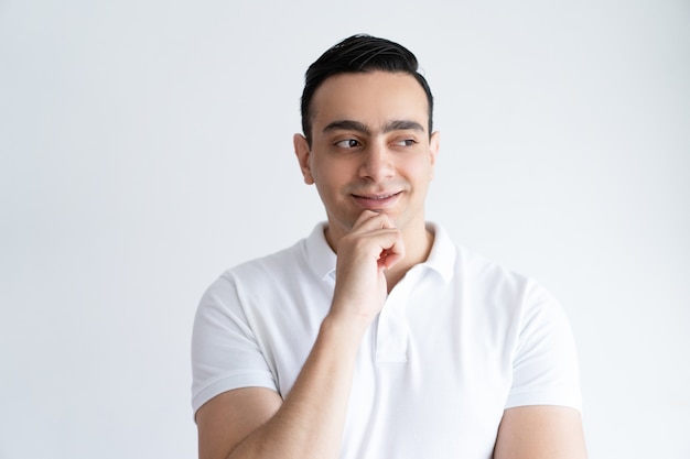 Jeune homme sournois touchant le menton et détournant les yeux. Beau mec pensant.