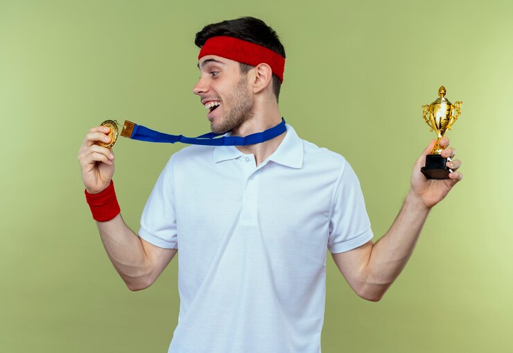 Photo gratuit jeune homme sportif en bandeau avec médaille d'or autour du cou tenant son trophée heureux et excité sur vert
