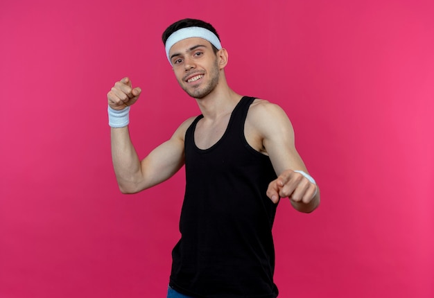 Jeune homme sportif en bandeau souriant pointant avec l'index debout sur le mur rose