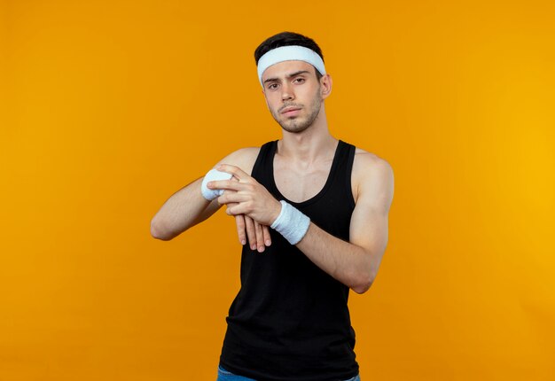 Jeune homme sportif en bandeau touchant son poignet étirant ses mains sur orange