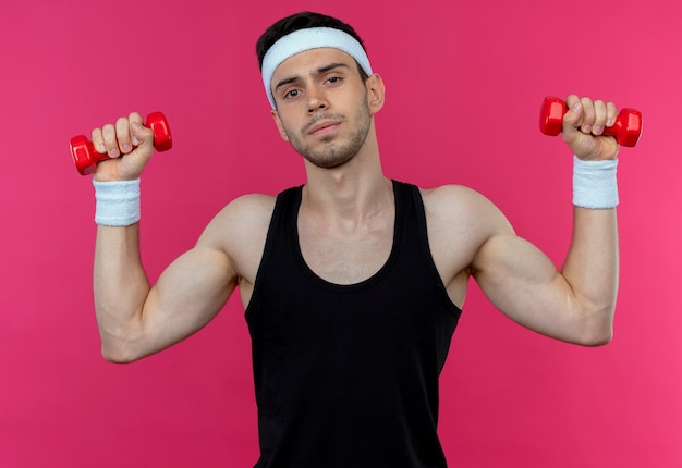 Jeune homme sportif en bandeau travaillant avec des haltères tendus et confiants sur rose