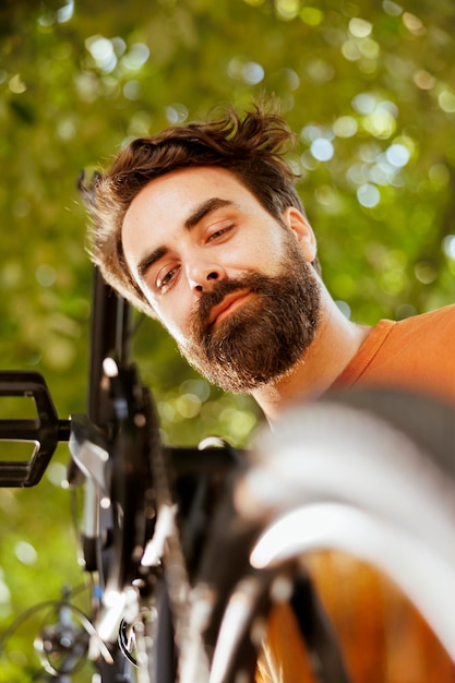 Photo gratuite jeune homme sportif examinant des pièces de vélo dans la cour de la maison pour des dommages à réparer avec des outils cycliste masculin énergique réparant une chaîne de vélo cassée et une roue à l'extérieur pour le vélo d'été