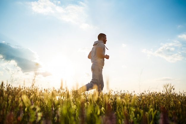 Jeune homme sportif jogging dans le champ au lever du soleil.