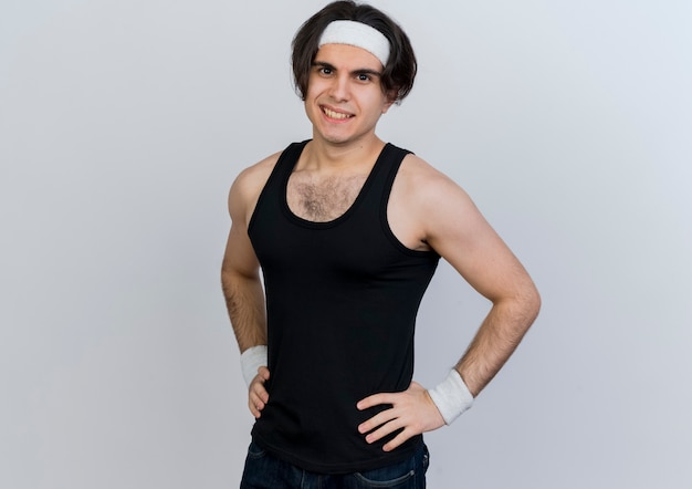Jeune homme sportif portant des vêtements de sport et un bandeau à l'avant souriant confiant debout sur un mur blanc