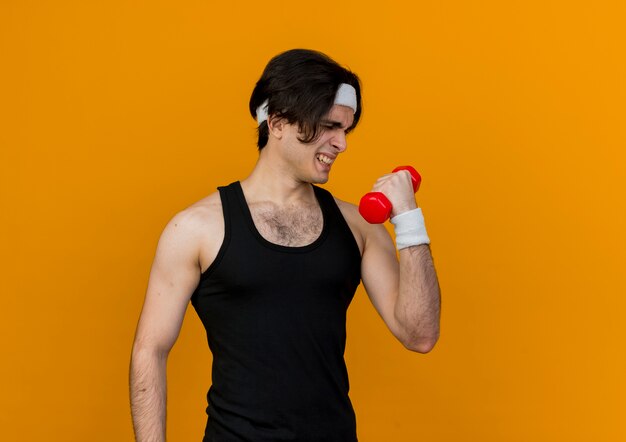 Jeune homme sportif portant des vêtements de sport et bandeau tenant haltère faisant des exercices à la recherche de tension