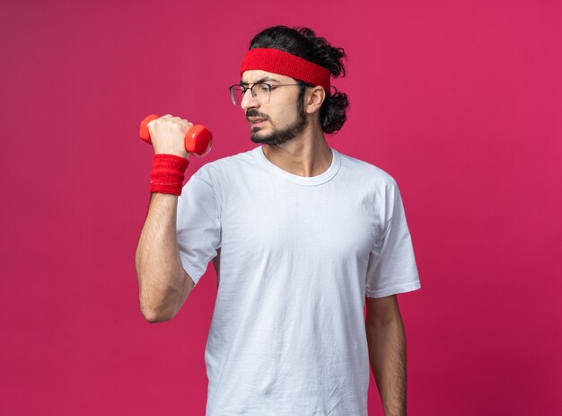 Jeune homme sportif tendu portant un bandeau avec un bracelet s'exécutant avec un haltère