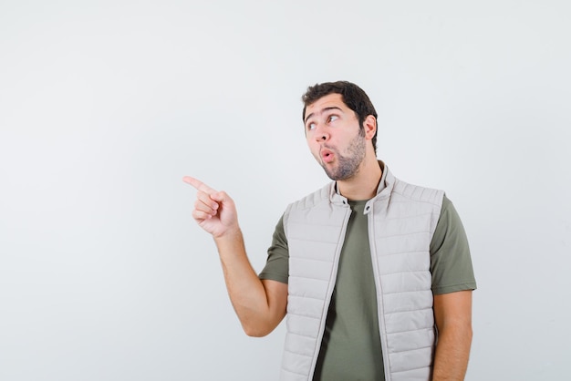 Jeune homme surprenant montrant la gauche avec son doigt sur fond blanc