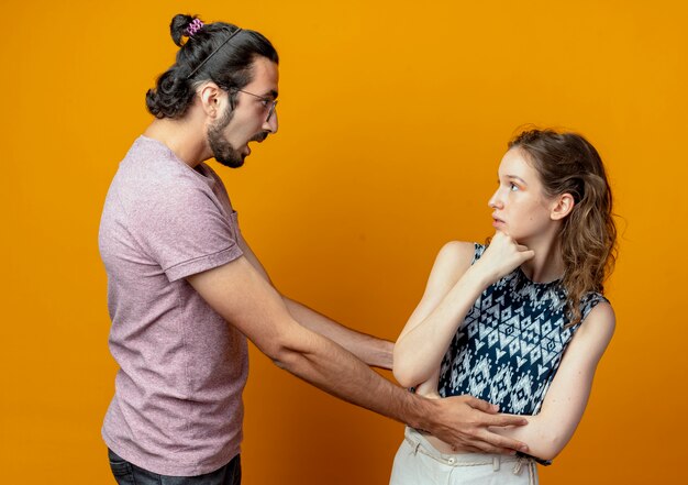 Jeune homme à la surprise de sa petite amie alors qu'elle le regarde perplexe sur le mur orange