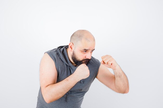 Jeune homme en sweat à capuche sans manches debout dans une pose de combat et l'air confiant, vue de face.