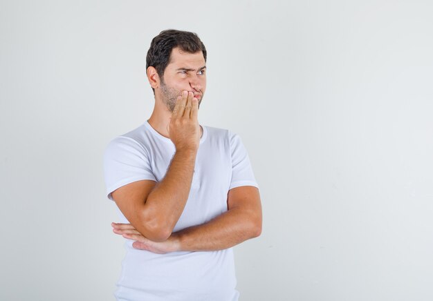 Jeune homme en t-shirt blanc debout avec la main près de la bouche et à la réflexion