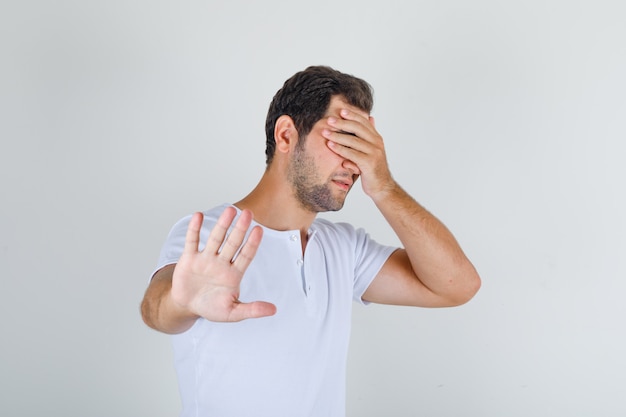 Jeune homme en t-shirt blanc faisant le geste d'arrêt et couvrant les yeux