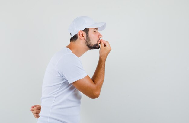 Jeune homme en t-shirt blanc montrant un geste délicieux et regardant concentré, vue de face.