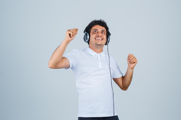 Jeune homme en t-shirt blanc montrant le geste du vainqueur et l'air heureux, vue de face.