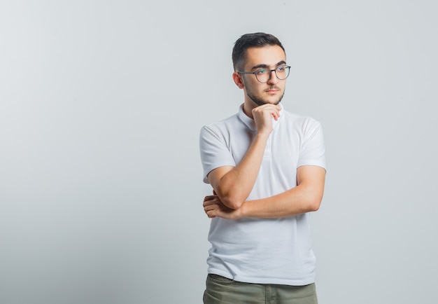 Jeune homme en t-shirt blanc, pantalon étayant le menton sur place et à la pensif