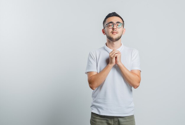 Jeune homme en t-shirt blanc, pantalon joignant les mains en geste de prière et à l'espoir