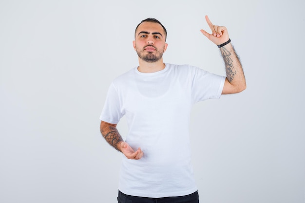 Jeune homme en t-shirt blanc et pantalon noir levant l'index en geste eurêka et l'air pensif