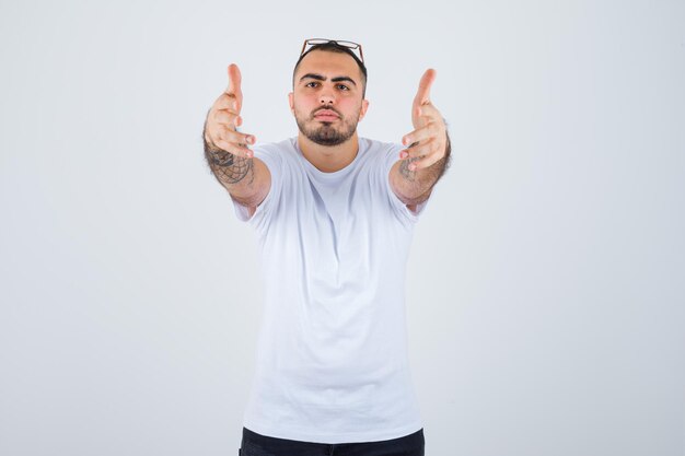 Jeune homme en t-shirt blanc et pantalon noir s'étirant les mains comme recevant quelque chose et ayant l'air sérieux