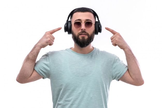 Jeune homme en t-shirt bleu avec barbe, écouter de la musique avec des écouteurs noirs