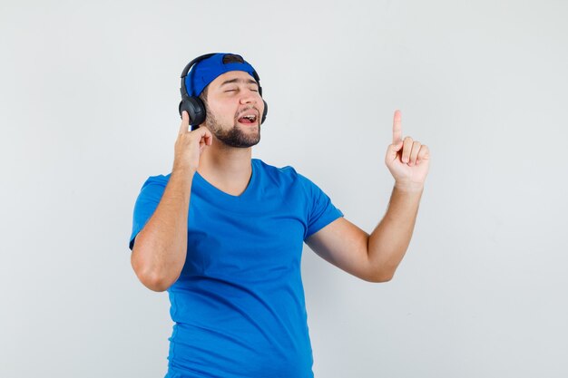 Jeune homme en t-shirt bleu et casquette appréciant la musique avec des écouteurs avec le doigt vers le haut