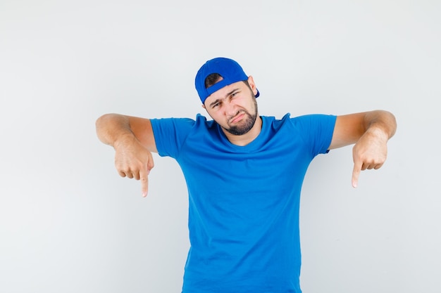 Jeune homme en t-shirt bleu et casquette pointant vers le bas et à la déception