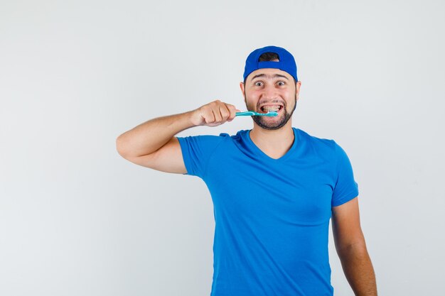 Jeune homme en t-shirt bleu et casquette se brosser les dents et à la positive