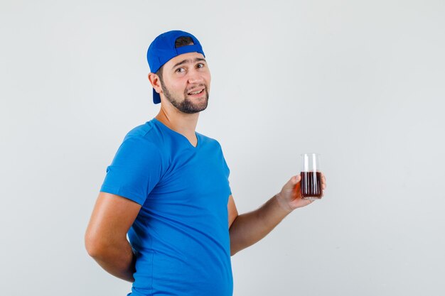 Jeune homme en t-shirt bleu et casquette tenant un verre de boisson gazeuse et à la recherche positive