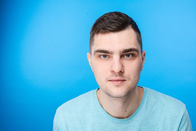 Un jeune homme en t-shirt bleu n'a pas d'émotions, photo isolée sur fond bleu